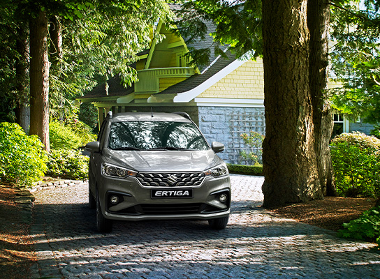 Silver-Suzuki-Ertiga-driving-on-a-road-with-trees-on-both-side