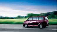 Side-view-of-a-purple-APV-driving-in-green-landscape