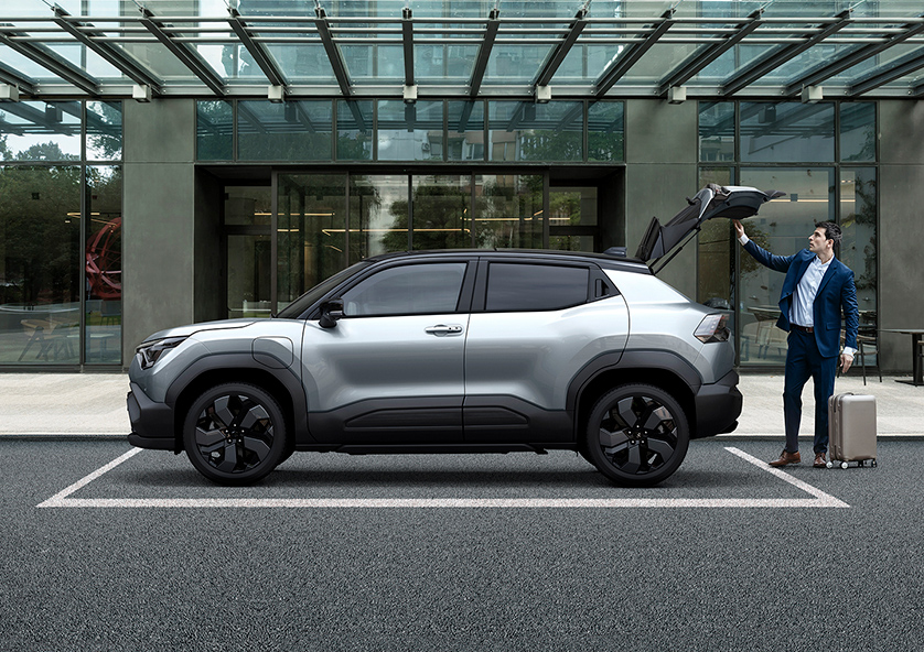 suzuki-e-vitara-parked-in-front-of-a-modern-building-with-person-opening-the-tailgate