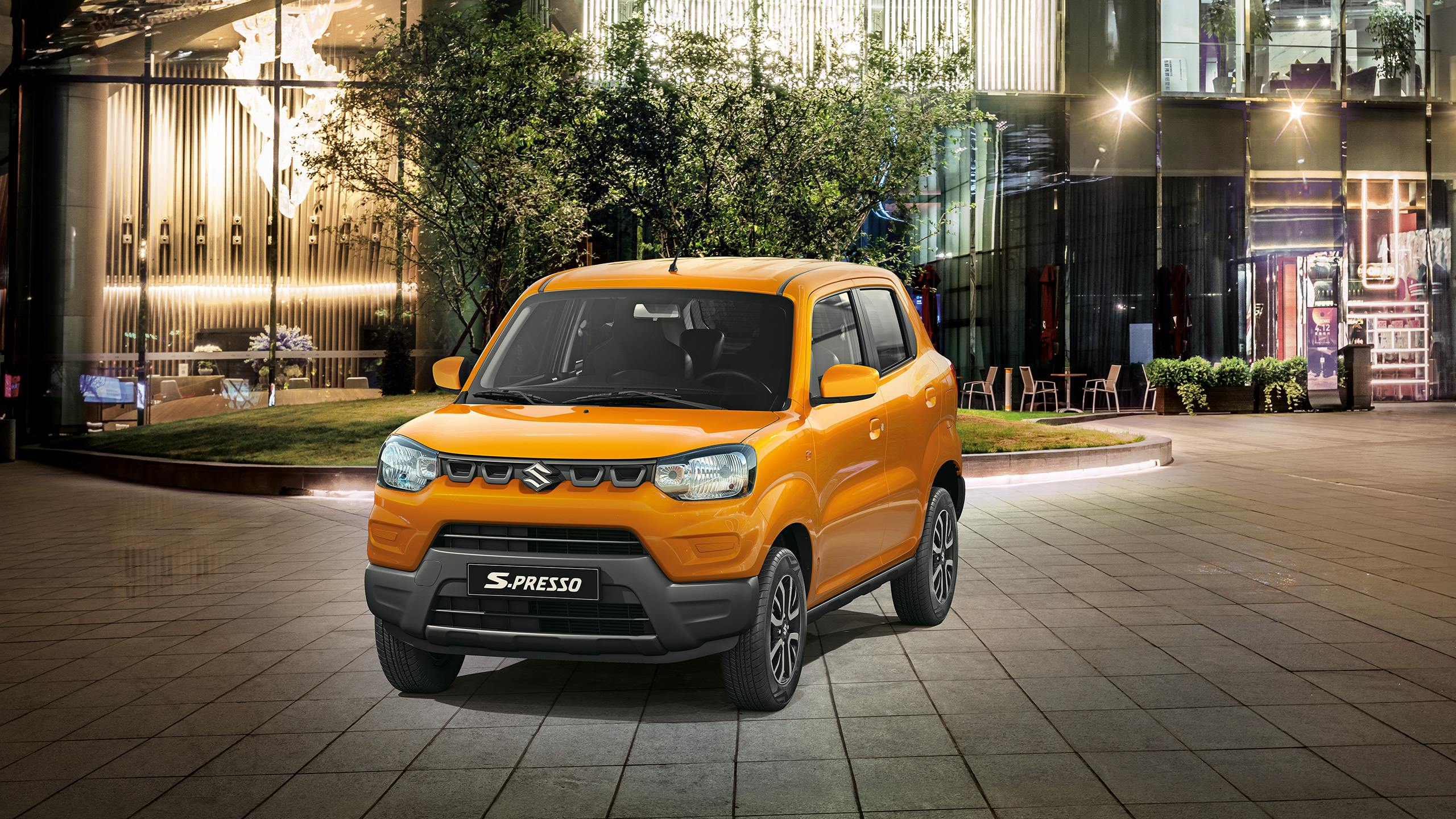 An orange S-PRESSO is parked in front of a glass building at night 